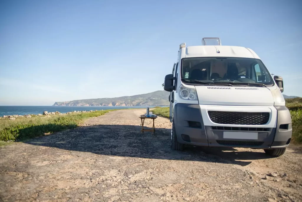 Camper van parked by ocean coastline under clear sky.