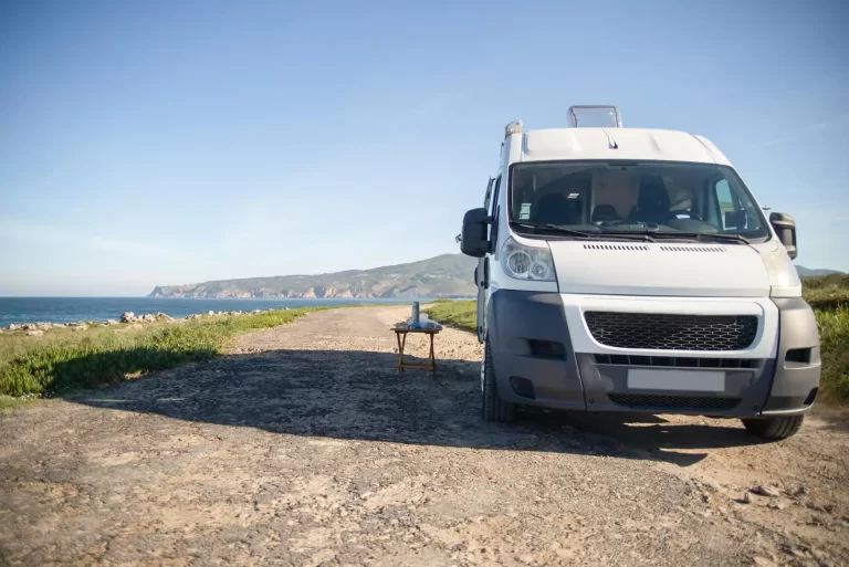 Camper van parked by ocean coastline under clear sky.